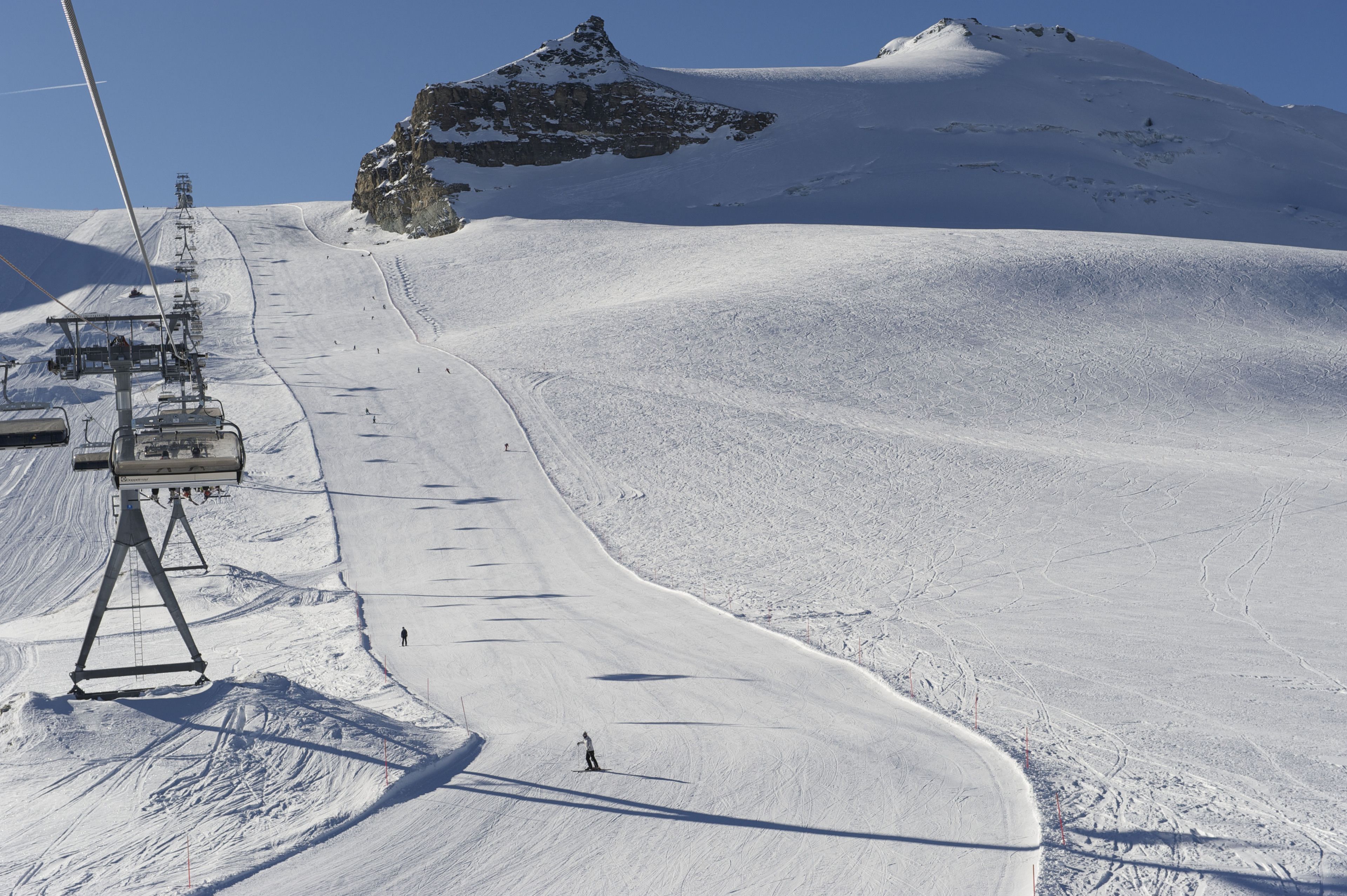 Pista de esquí cubierta de nieve, con un telesilla y una cima montañosa al fondo.