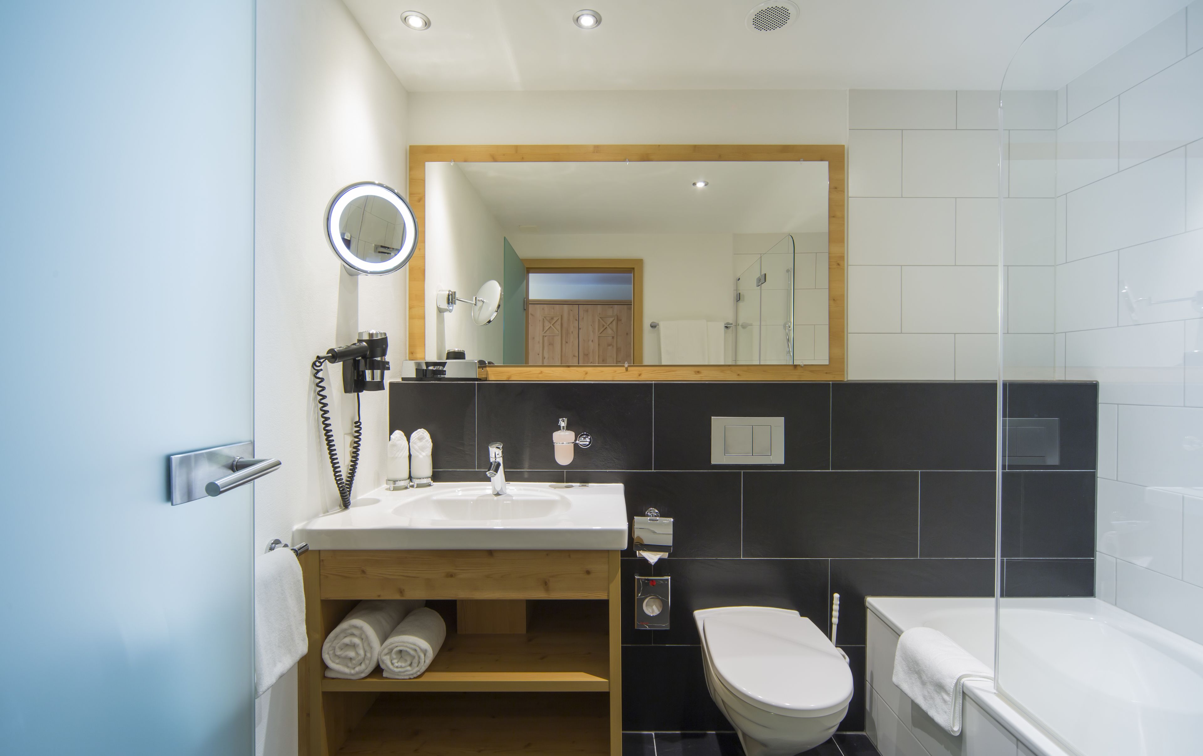 Un baño moderno con un mueble de tocador de madera, un espejo redondo, un inodoro y una bañera.