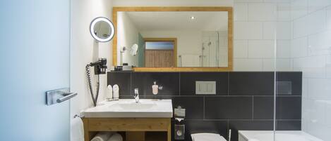 A modern bathroom with a wooden vanity, a round mirror, a toilet, and a bathtub.