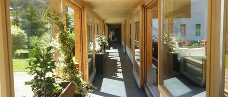 A corridor with wooden walls and large windows, leading to a room with a bed and a view of a garden.