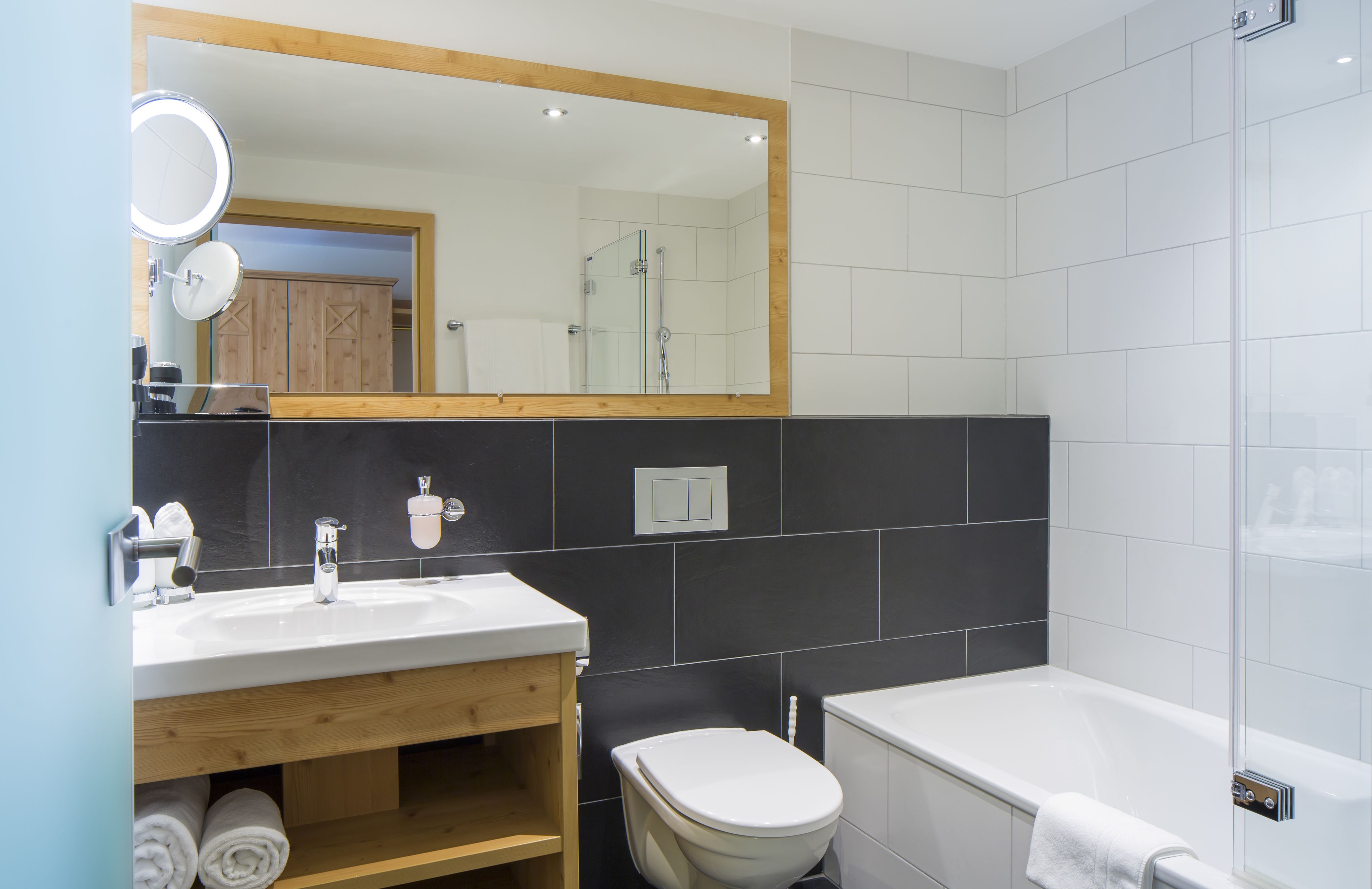 Un bany modern amb un lavabo blanc, un tocador de fusta, un vàter i una dutxa amb envà.