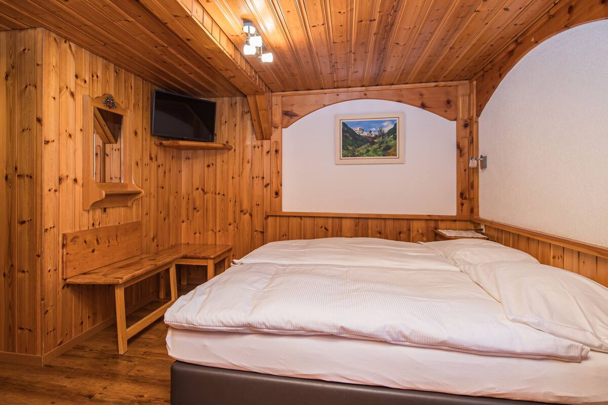 A wooden-paneled room with a bed, a bench, a mounted TV, and a framed picture on the wall.