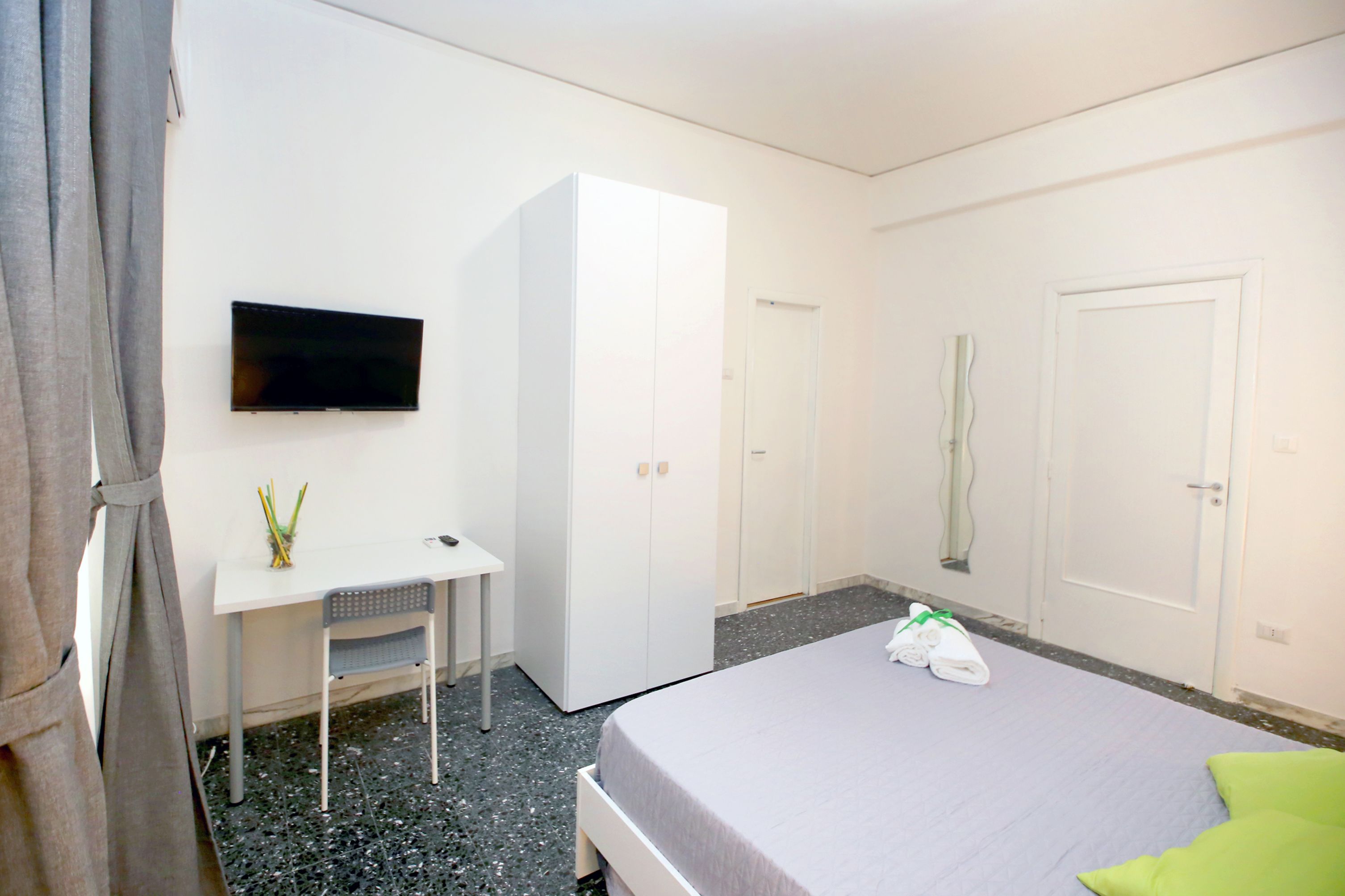 Ein Hotelzimmer mit Bett, Schreibtisch, Kleiderschrank, Fernseher und einer Tür.
