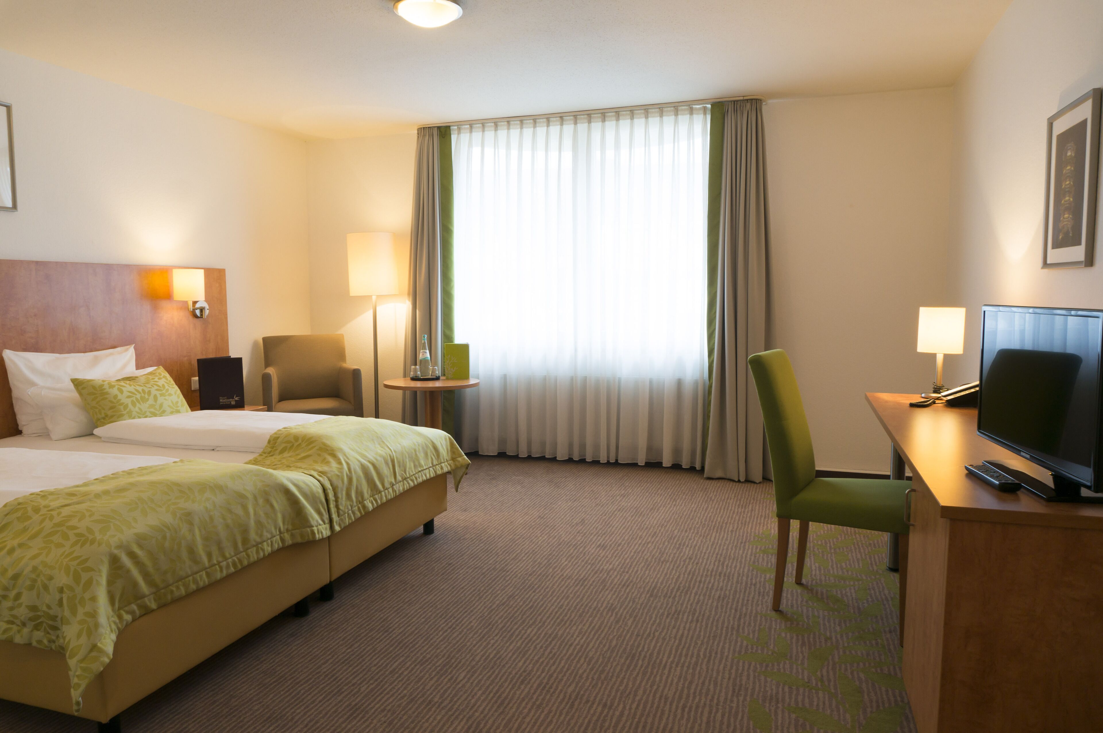 Habitación de hotel con dos camas, un escritorio, televisor, una silla y una ventana con cortinas.
