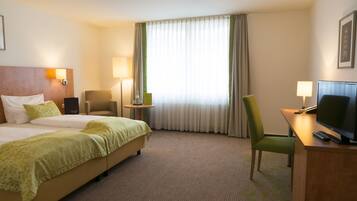 Habitación de hotel con dos camas, un escritorio, televisor, una silla y una ventana con cortinas.