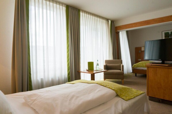 Una habitación de hotel con cama, una silla, escritorio con televisor y ventana con cortinas.