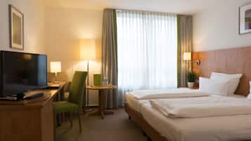 Habitación de hotel con cama, dos mesitas de noche, televisión, una silla, lámpara y ventana con cortinas.