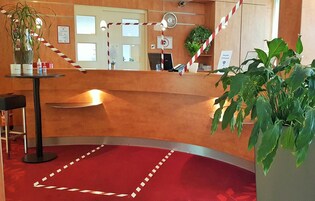 A reception area with a curved counter, red carpet, potted plants, a desk lamp, and informational signs.