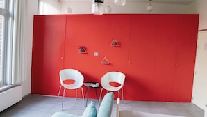 A room with a red partition, two white chairs, a small table, and a window with white curtains. - Vegan b&b AM/PM (Bruges)