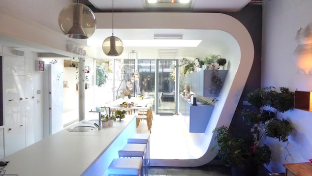 A modern kitchen with a curved island, pendant lighting, and a view into the dining area. - Vegan b&b AM/PM (Bruges)