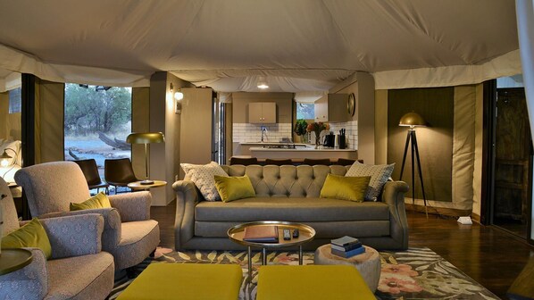 A tented accommodation with a sofa, armchairs, a small table, and a kitchen area visible through the windows.