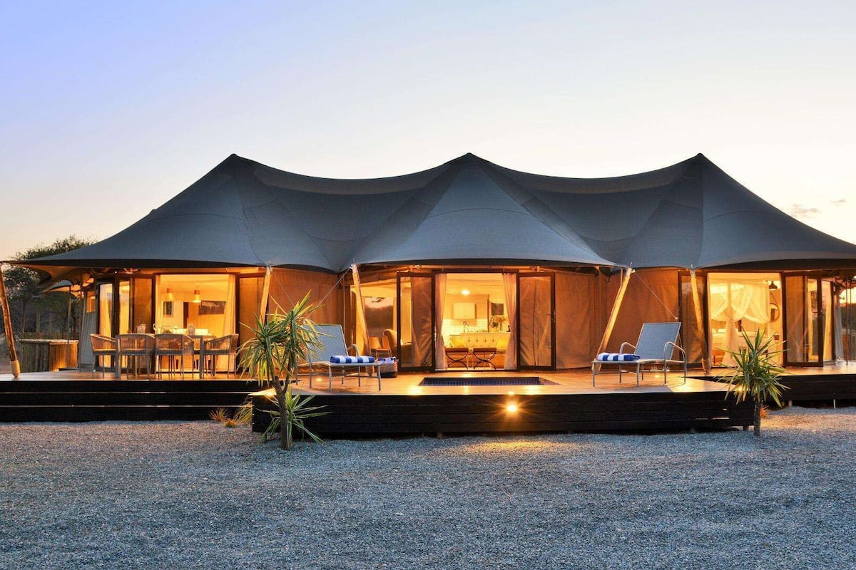 Alojamiento moderno con carpa, zona de comedor, sillones y piscina.