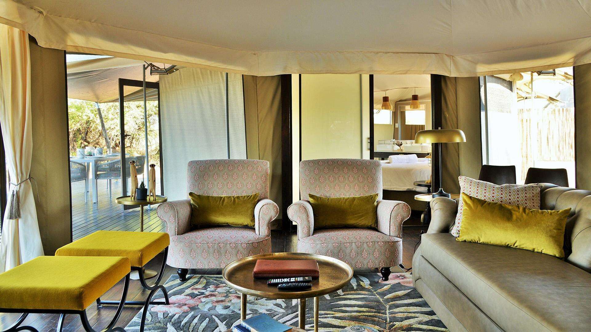 Un salon chaleureux avec deux fauteuils à motifs, un canapé, une petite table basse et un pouf jaune.