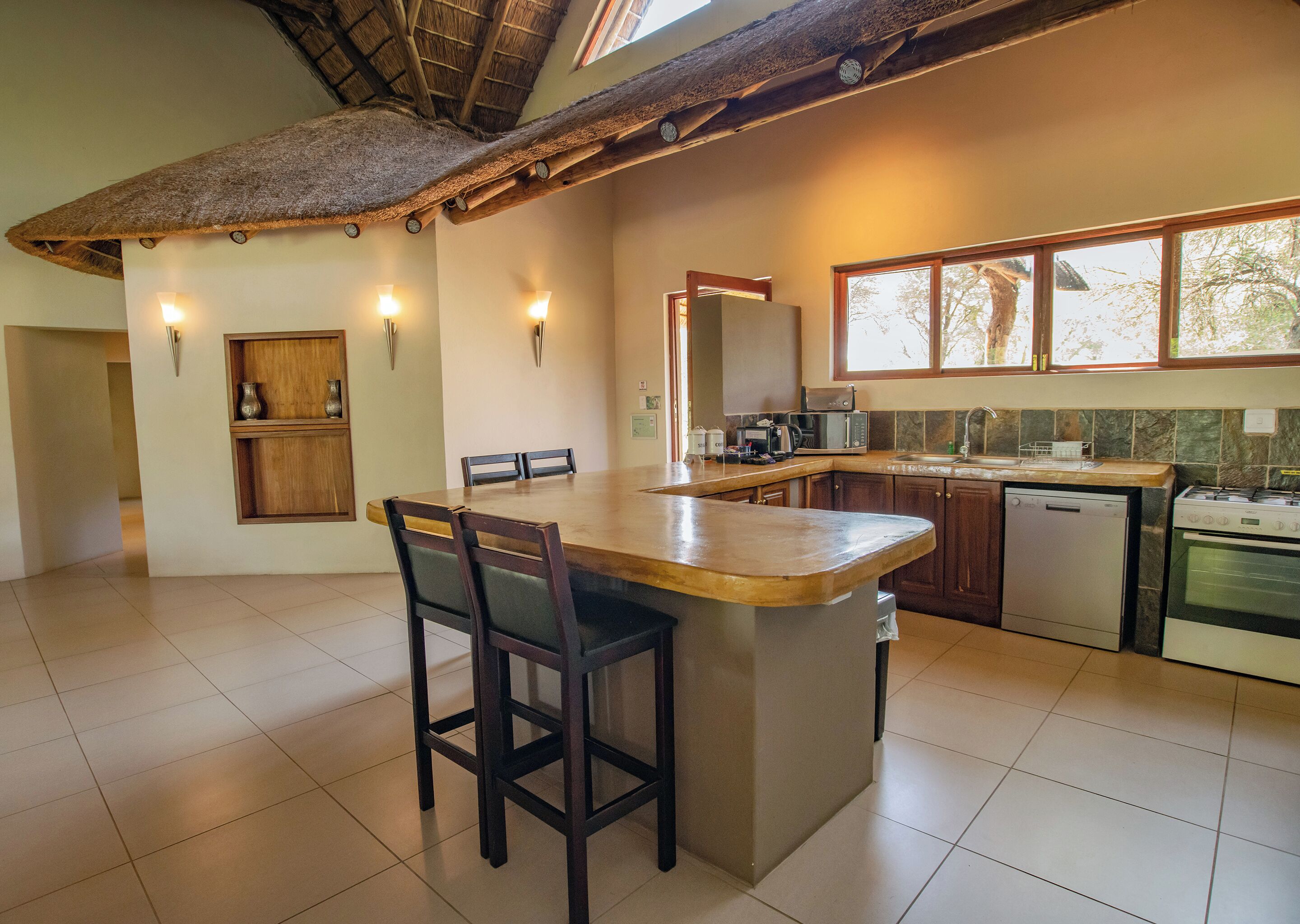 A spacious kitchen with a large island, wooden cabinets, and a thatched ceiling.
