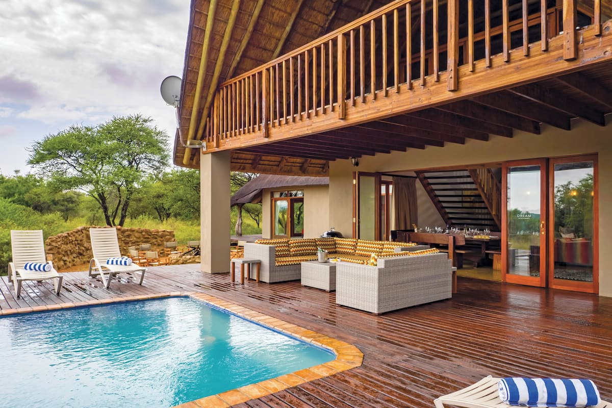 Un área de piscina con muelle de madera, sillas de descanso y una zona de estar con sofá y mesa.