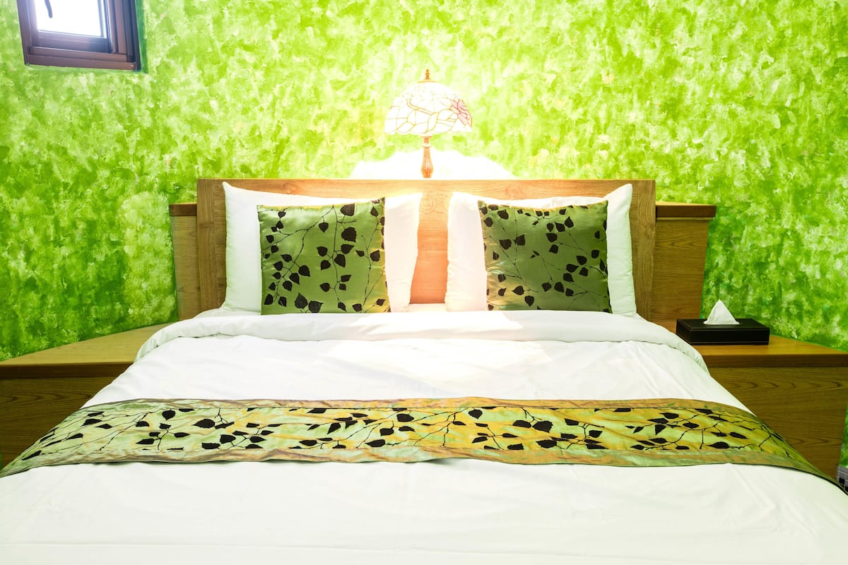 Een bed met witte beddengoed en een plaid met bladprint, voor een groen, gestructureerde muur.