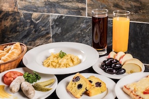 A breakfast setting with various dishes including eggs, sausages, bread, and fruit.