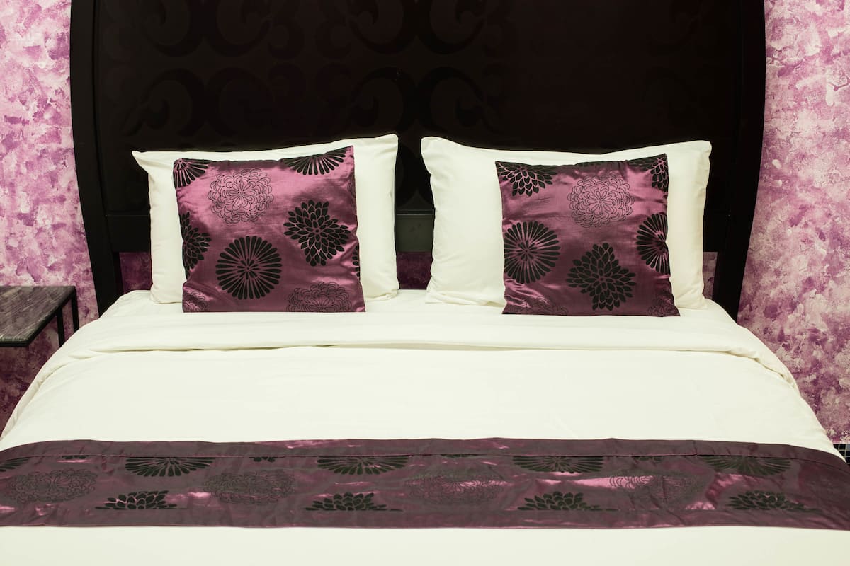 Een bed met wit beddengoed en twee sierkussens met een bloemenmotief.