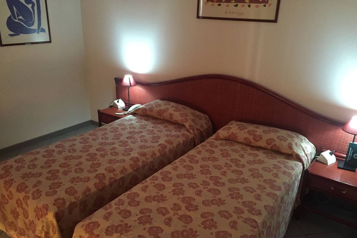 Une chambre avec deux lits, chacun agrémenté de draps à motifs floraux, une table de chevet avec une lampe et une œuvre d  ’art encadrée au mur.