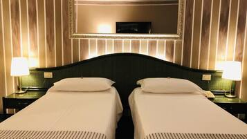 Camera d'albergo con due letti, un grande specchio sopra e lampade da comodino.