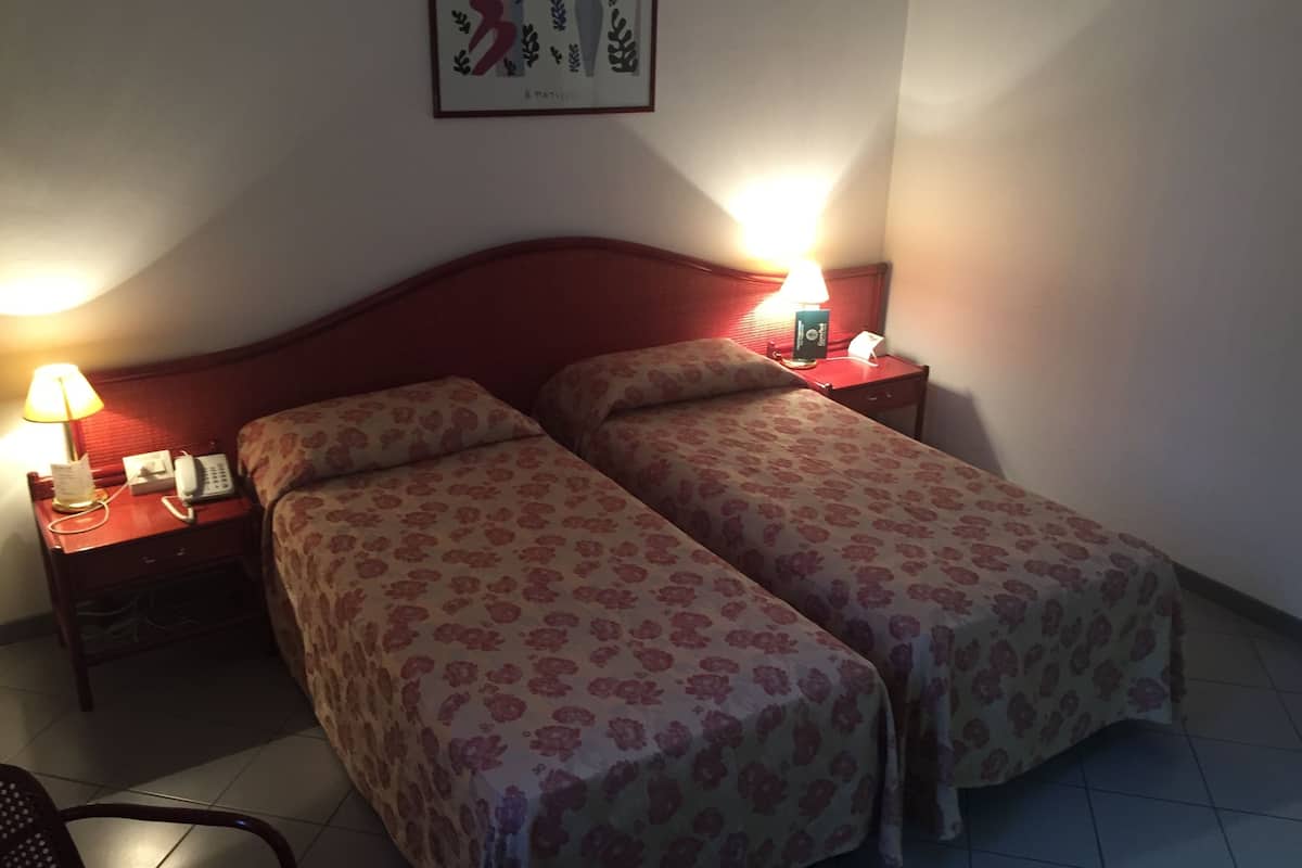 Une chambre d’hôtel avec deux lits, une table de chevet avec une lampe, un téléphone et un tableau encadré au mur.