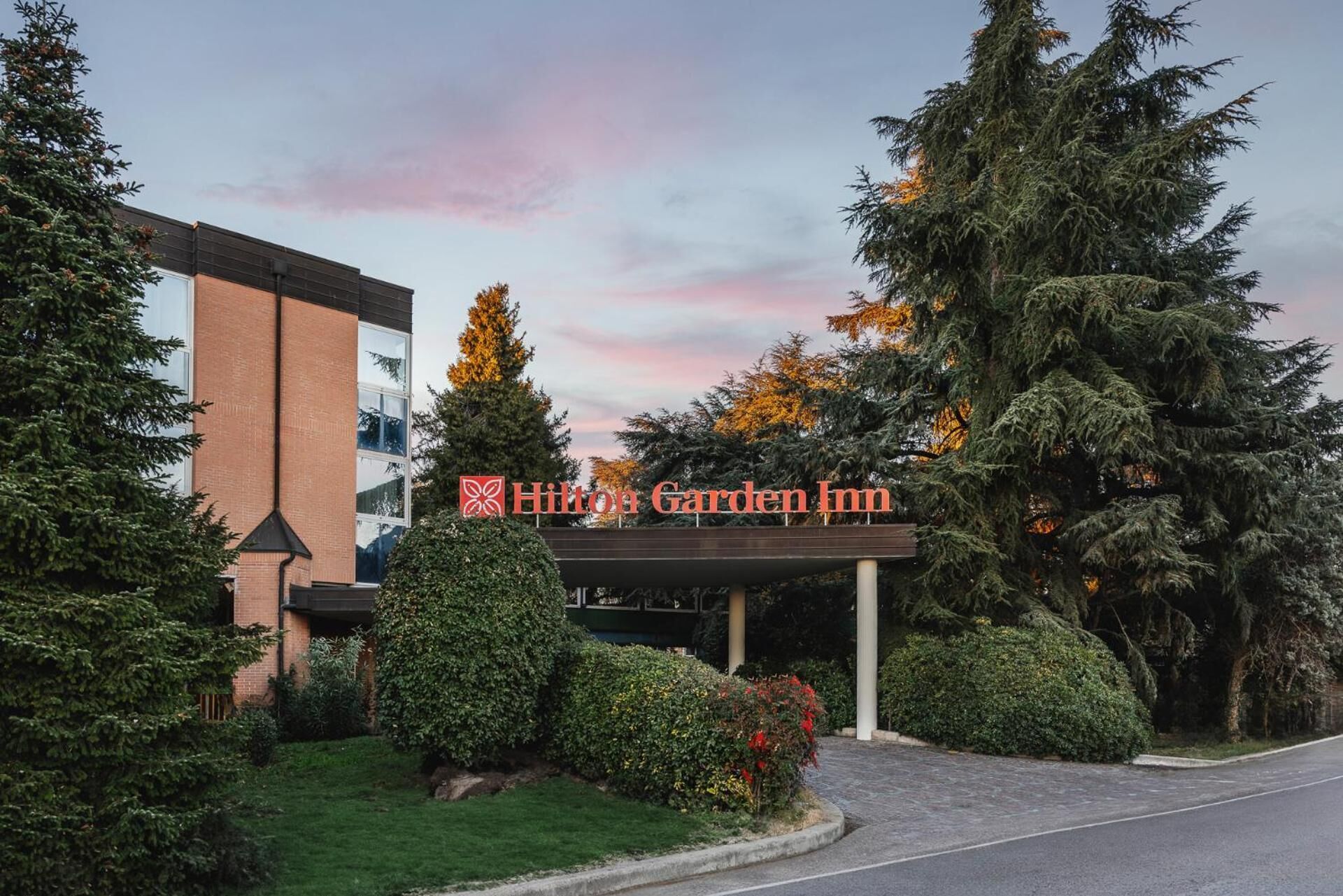L'esterno del Hilton Garden Inn, con una chiara vista dell'ingresso dell'edificio, una tettoia e vegetazione circostante.