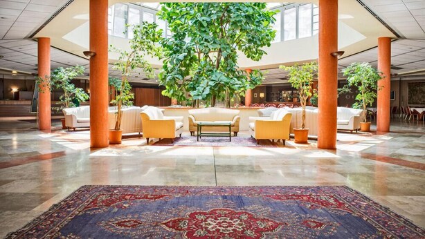 A spacious lobby with a large central tree, comfortable seating, and a patterned carpet. - Green Park Bologna Residence (Granarolo dell'Emilia)