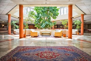 Een ruime lobby met een grote centrale boom, comfortabele zitplaatsen en een kamerbreed tapijt met een patroon.