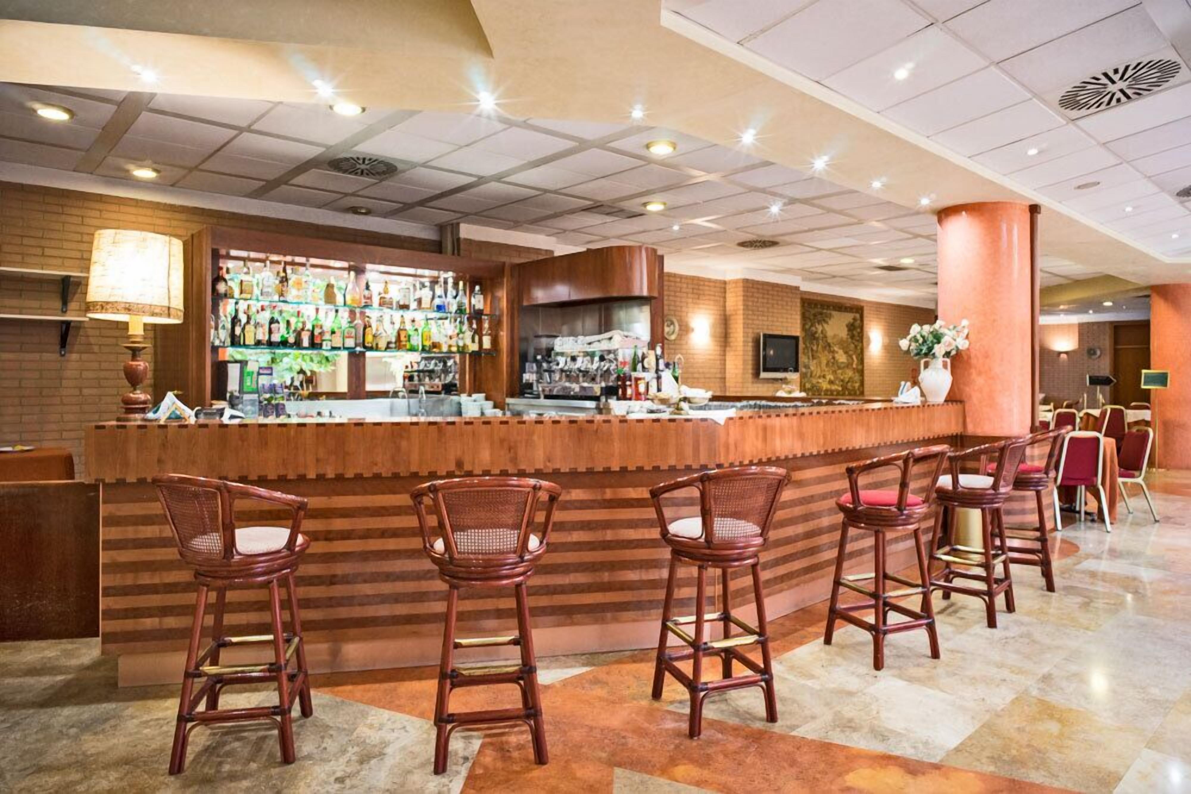 Angolo bar con un bancone in legno, diversi sgabelli da bar e una varietà di bottiglie sugli scaffali.