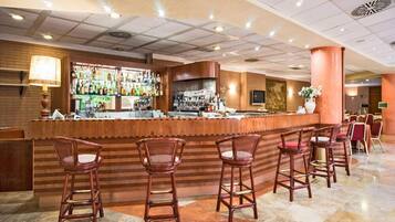 Angolo bar con un bancone in legno, diversi sgabelli da bar e una varietà di bottiglie sugli scaffali.