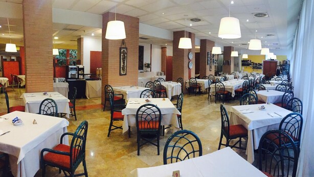 Un restaurante con varias mesas y sillas, pilares de ladrillo y lámparas colgantes.
