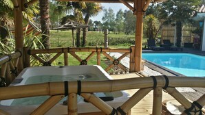 Kuumavesiallas bambusta rakennetussa huvimajassa, josta on näkymä uima-altaalle.