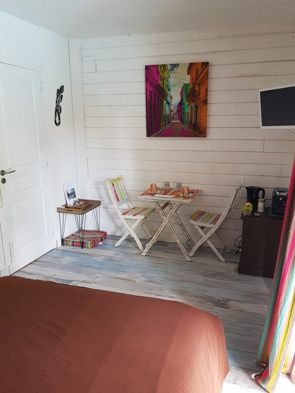 Una habitación con cama, una mesa pequeña con sillas, un cuadro en la pared y un escritorio con silla.