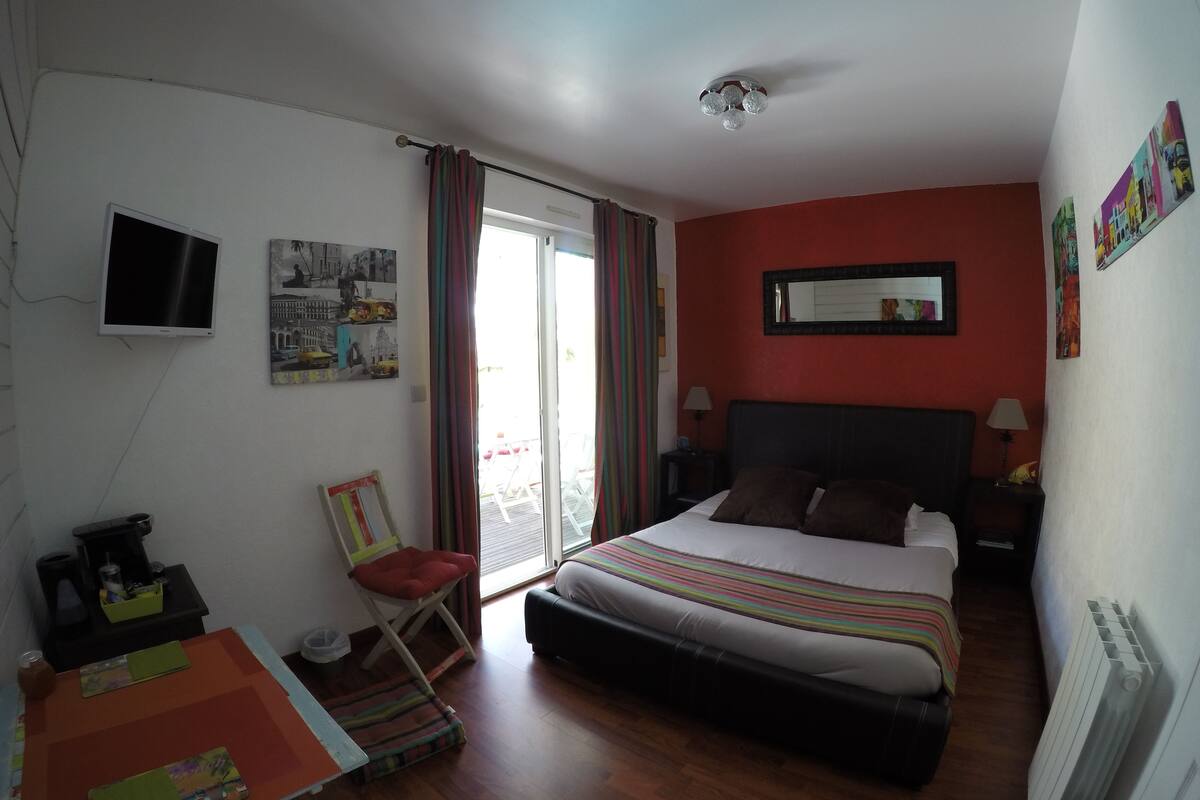 A hotel room with a bed, a desk, a chair, a TV, and a window with curtains.