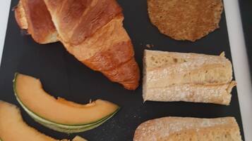 Verschiedene Speisen, darunter Croissants, Brot und Melonenscheiben, sind auf einer schwarzen Platte angerichtet.