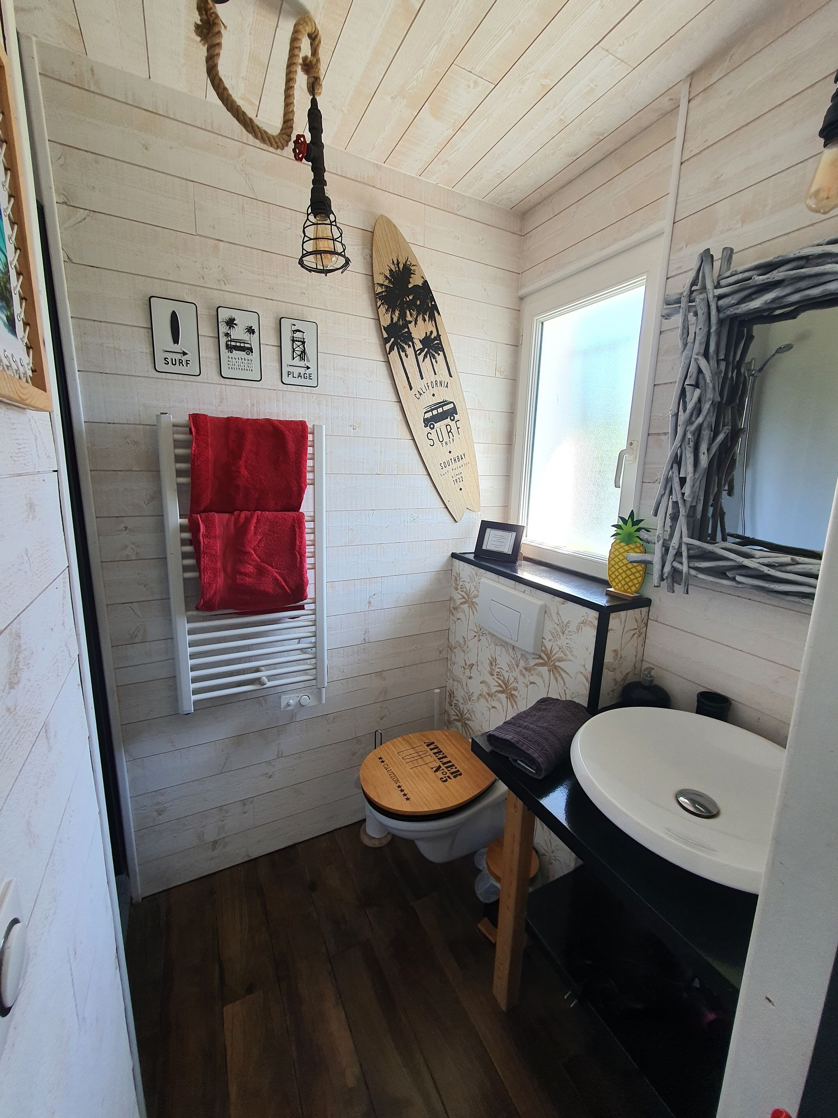 A compact bathroom with a wooden floor, a white toilet with a wooden seat, a white sink, and a red towel hanging on a white radiator.