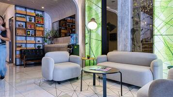 A modern lobby with a sofa, armchairs, a coffee table, a bookshelf, and a green decorative wall.
