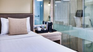 Una habitación de hotel moderna con cama, mesita de noche y zona de ducha con vidrio.