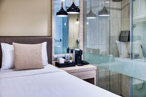 Una habitación de hotel moderna con cama, mesita de noche y zona de ducha con vidrio.