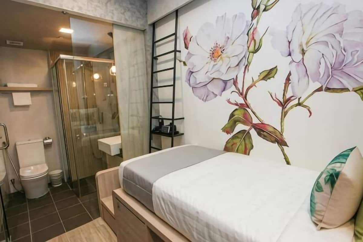 A bedroom with a bed, a shower, a toilet, and a wall with a floral mural.