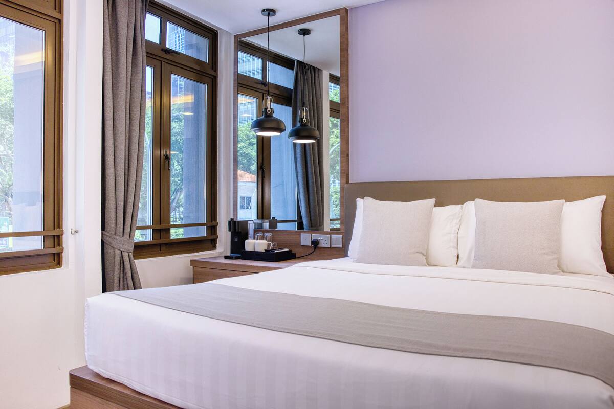 A hotel room with a large bed, a bedside table with a coffee maker, and a mirror above the bed.
