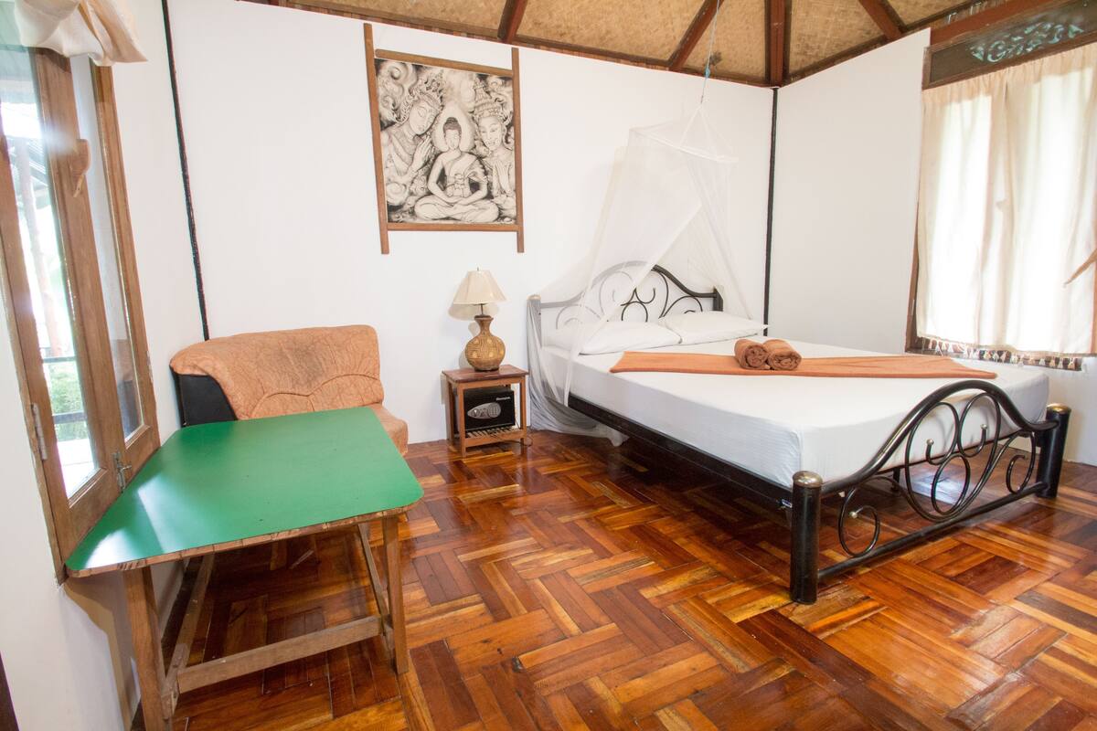 Une pièce comprenant un lit, une chaise, une petite table, une lampe et un tableau accroché au mur.