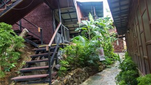 A narrow stone pathway flanked by lush greenery and a staircase leading to a building with a metal framework.
