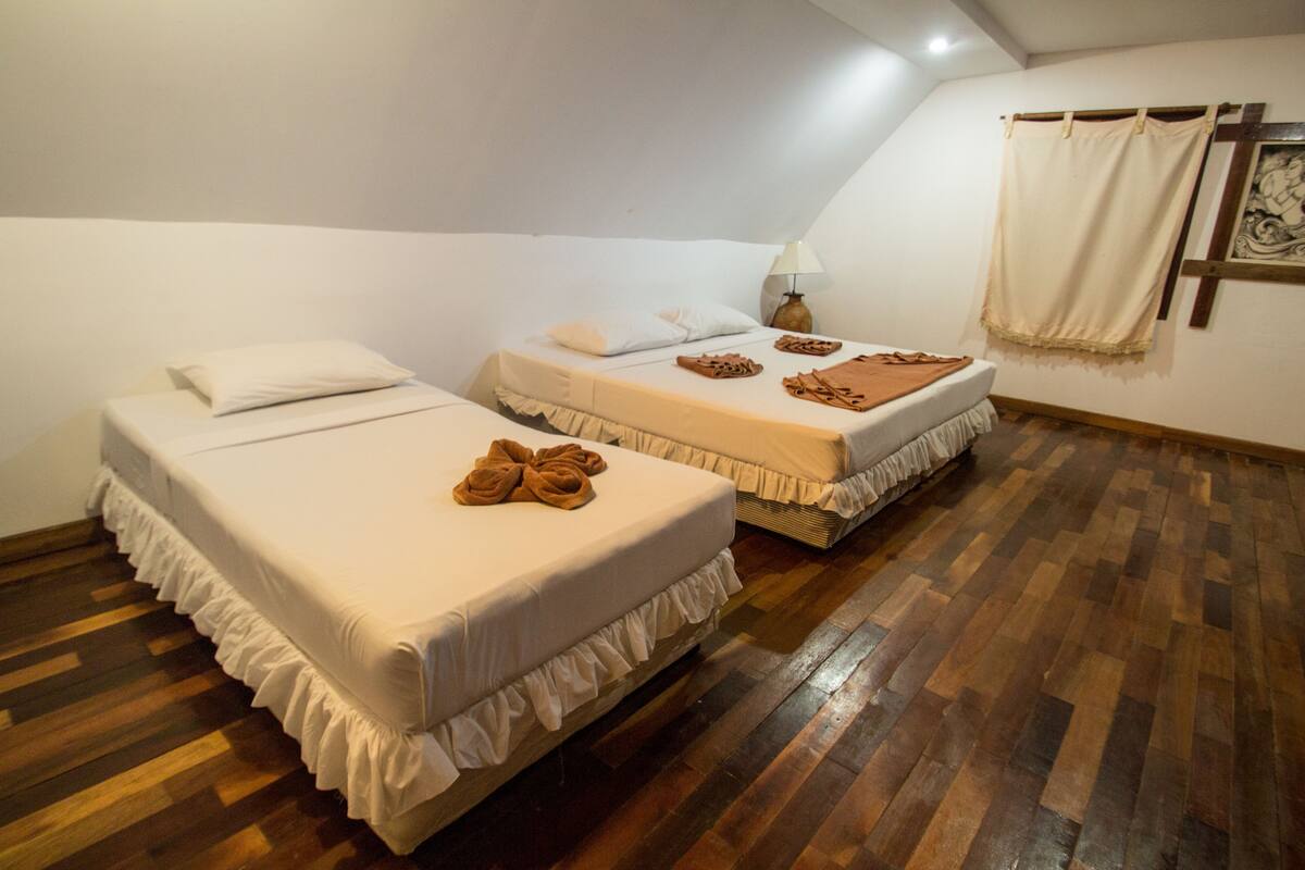 Une chambre avec deux lits, un plancher en bois et un luminaire au plafond.