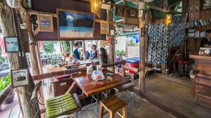 An outdoor restaurant with wooden furniture, a bar area, and various decorations including framed pictures and a signboard.
