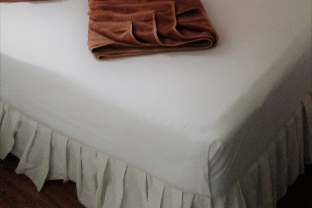 Un lit simple avec du linge de lit blanc, un ciel de lit blanc et deux serviettes marron pliées posées sur le lit.