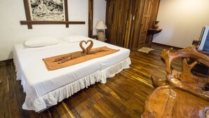 A neatly made bed with a heart-shaped towel, a wooden floor, a wall-mounted air conditioner, and a wooden wardrobe.