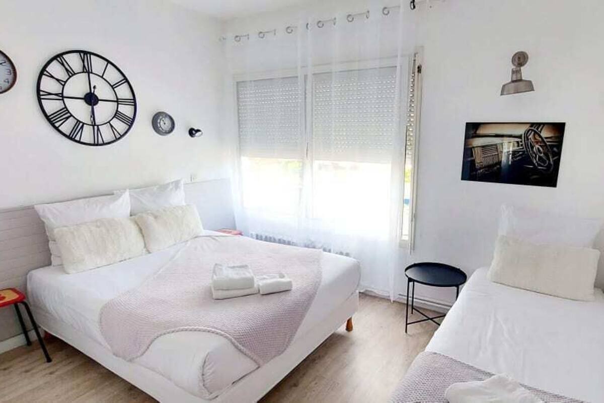 Un dormitorio con una cama grande, una cama más pequeña, una mesita de noche, una silla y una ventana con persianas.
