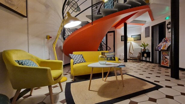 Un moderno vestíbulo de hotel con un sofá amarillo, un sillón amarillo, una mesa redonda y una escalera de caracol.
