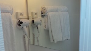 Un baño con lavamanos blanco, espejo, secador de pelo y toallero.